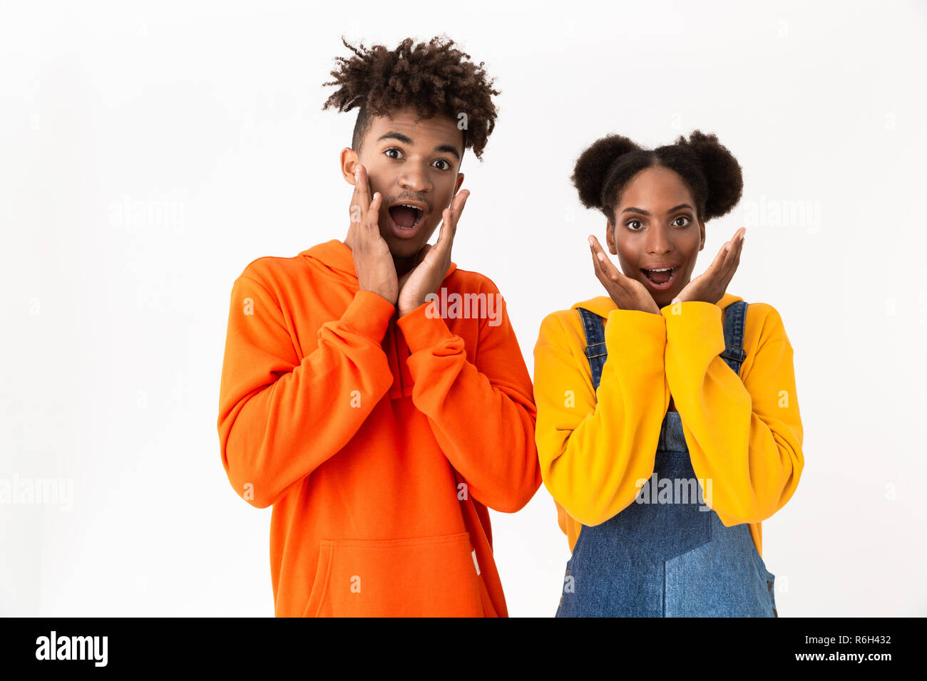 Immagine di entusiasti americano africano giovane in abiti colorati urlando e toccando le guance isolate su sfondo bianco Foto Stock