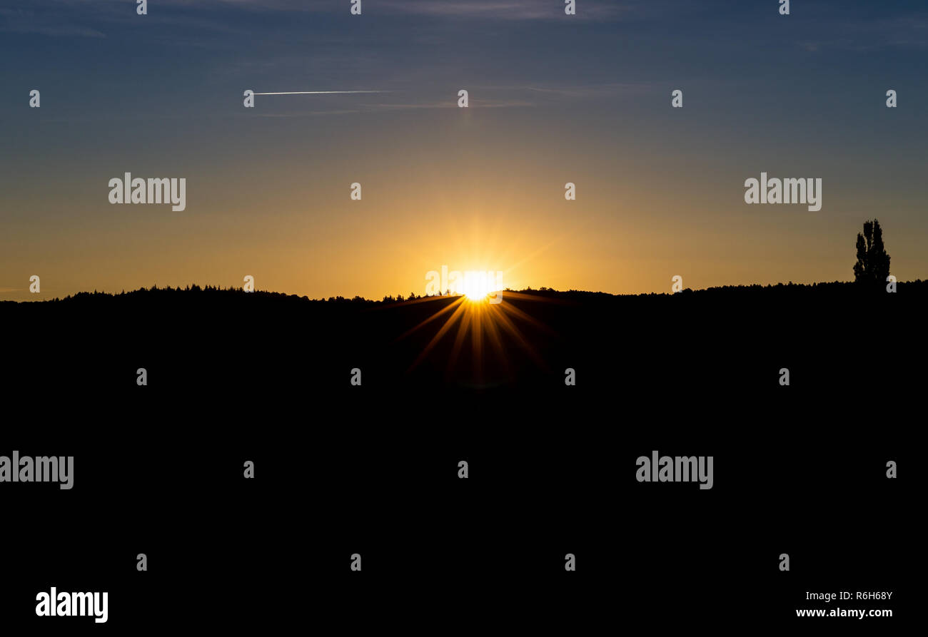 Mattina scena del sorgere del sole come forma a stella dal bordo di silhouette collina ricoperta dalla bussola e piccolo albero con il blu del cielo. Foto Stock