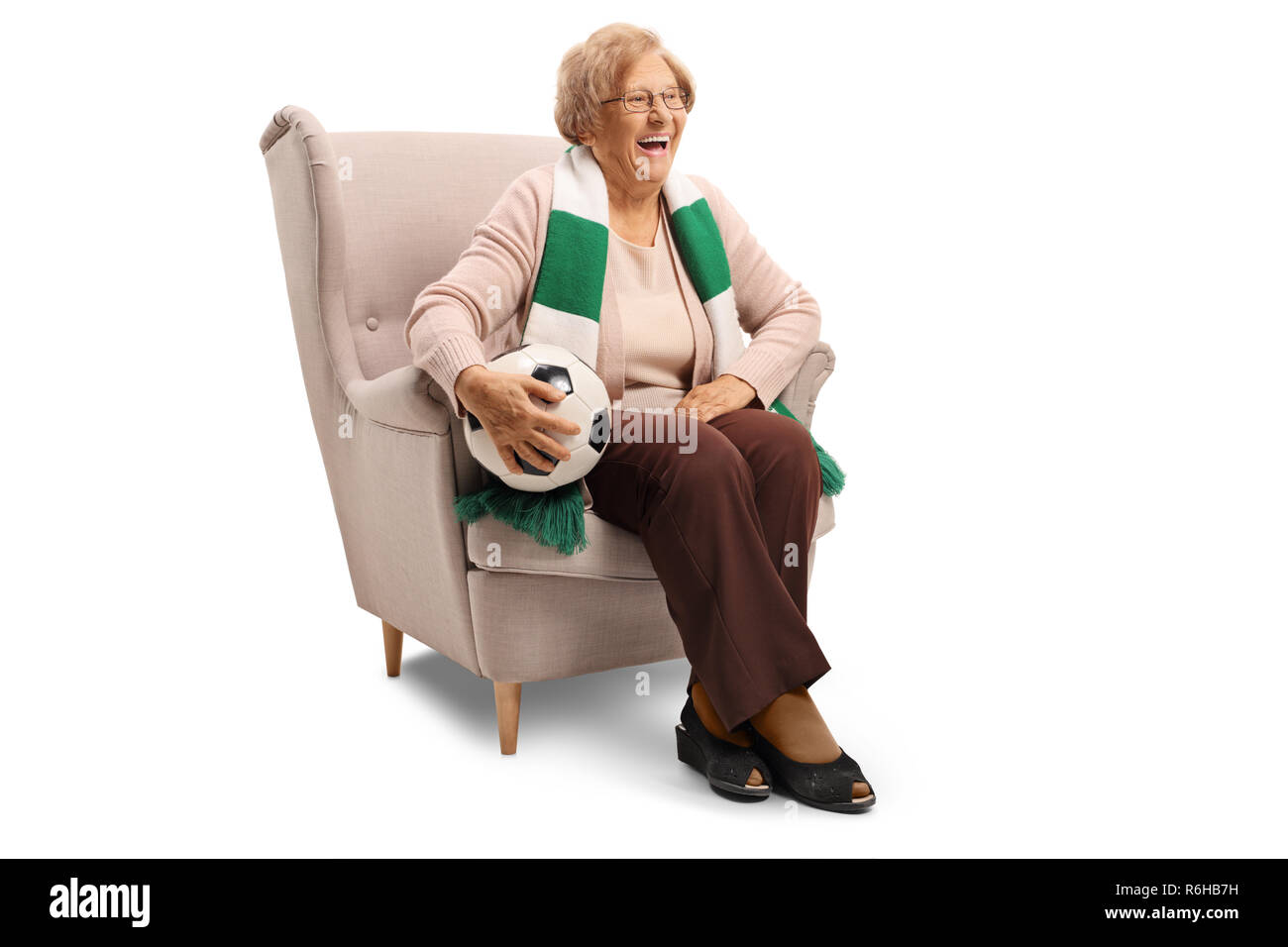 Felice senior donna seduta in una poltrona con un pallone da calcio e un foulard isolati su sfondo bianco Foto Stock