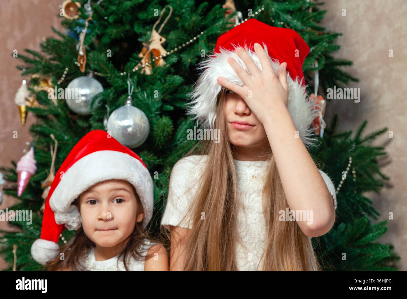 Due amiche sono in posa e ingannare intorno al Nuovo Anno Albero vicino al camino in una lussuosa dimora in buffi cappelli rossi. Il concetto di st Foto Stock