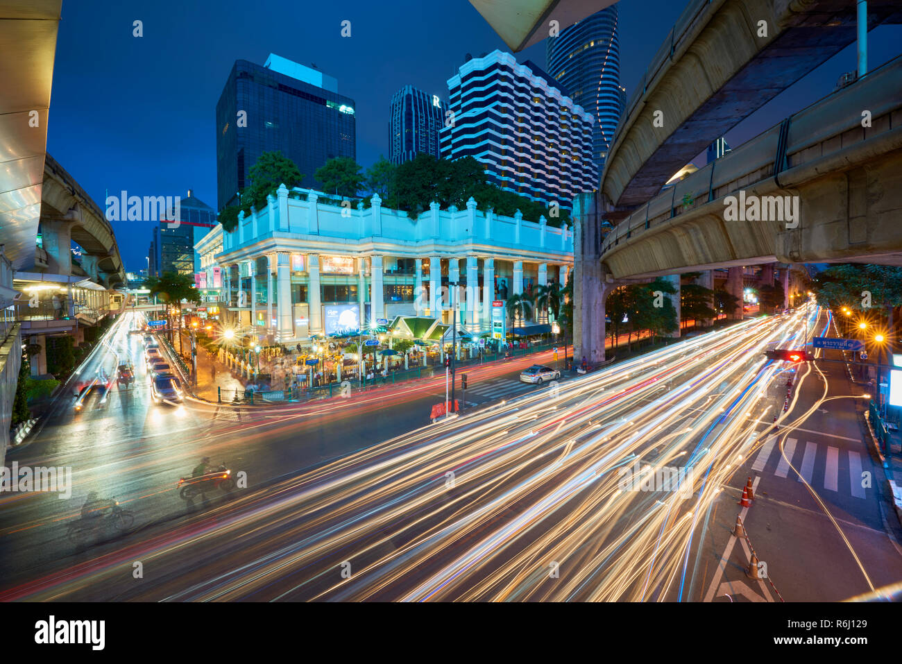 Creative elevato angolo night shot di Ratchaprasong intersezione e Santuario di Erawan a Bangkok, Thailandia, con la luce colorata sentiero da Cars driving passato Foto Stock