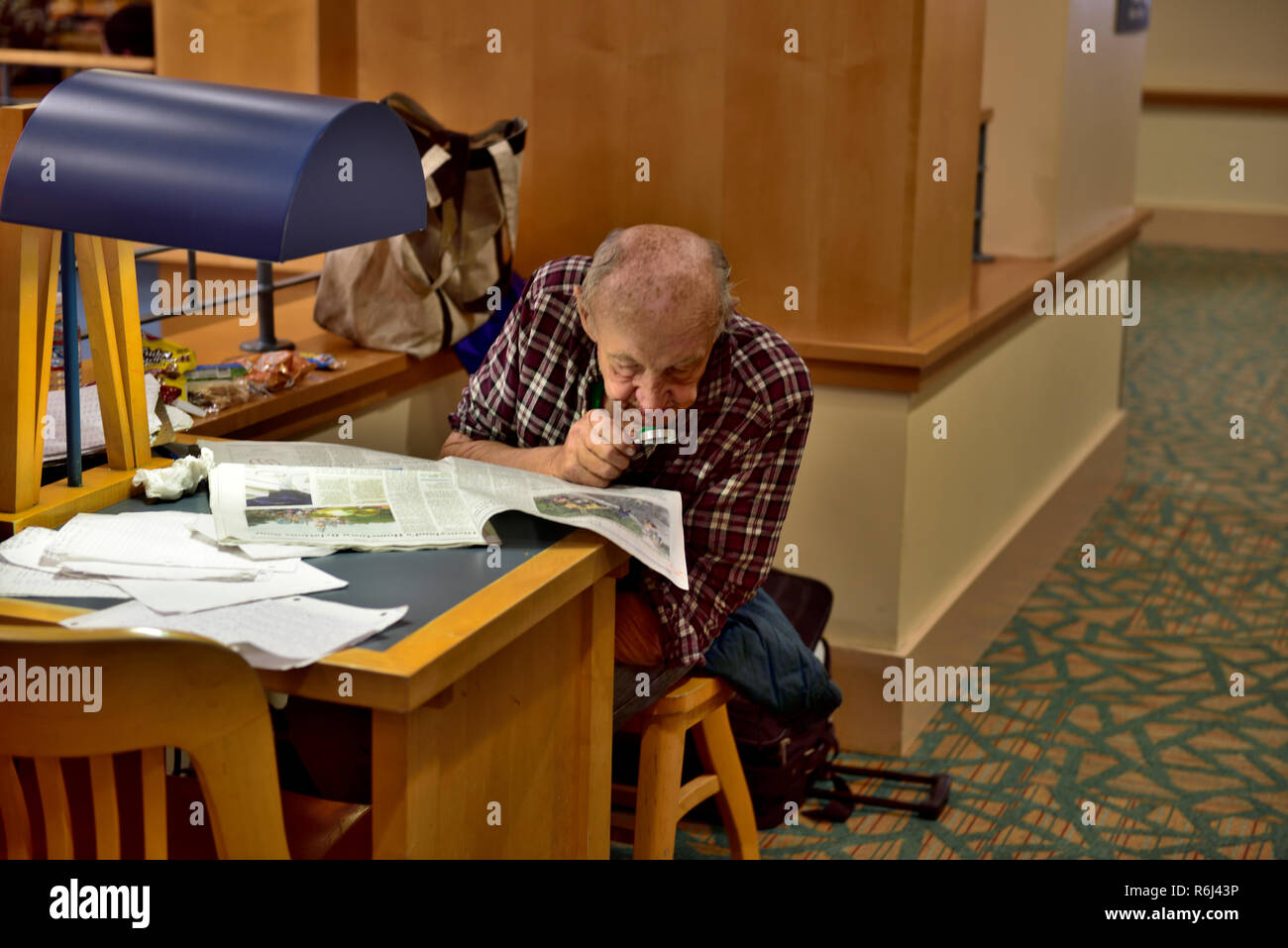 Uomo più anziano di lettura, lo studio quotidiano con lente di ingrandimento a scrivania in biblioteca pubblica Foto Stock