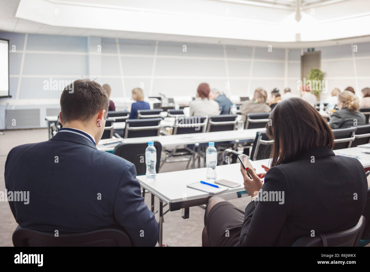 Business uomo e donna con e persone in ascolto sulla conferenza o sulla formazione nella hall Foto Stock