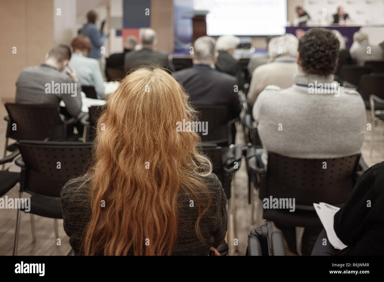 Business donna bionda con i capelli lunghi e le persone in ascolto sulla Conferenza o sulla formazione nella hall Foto Stock