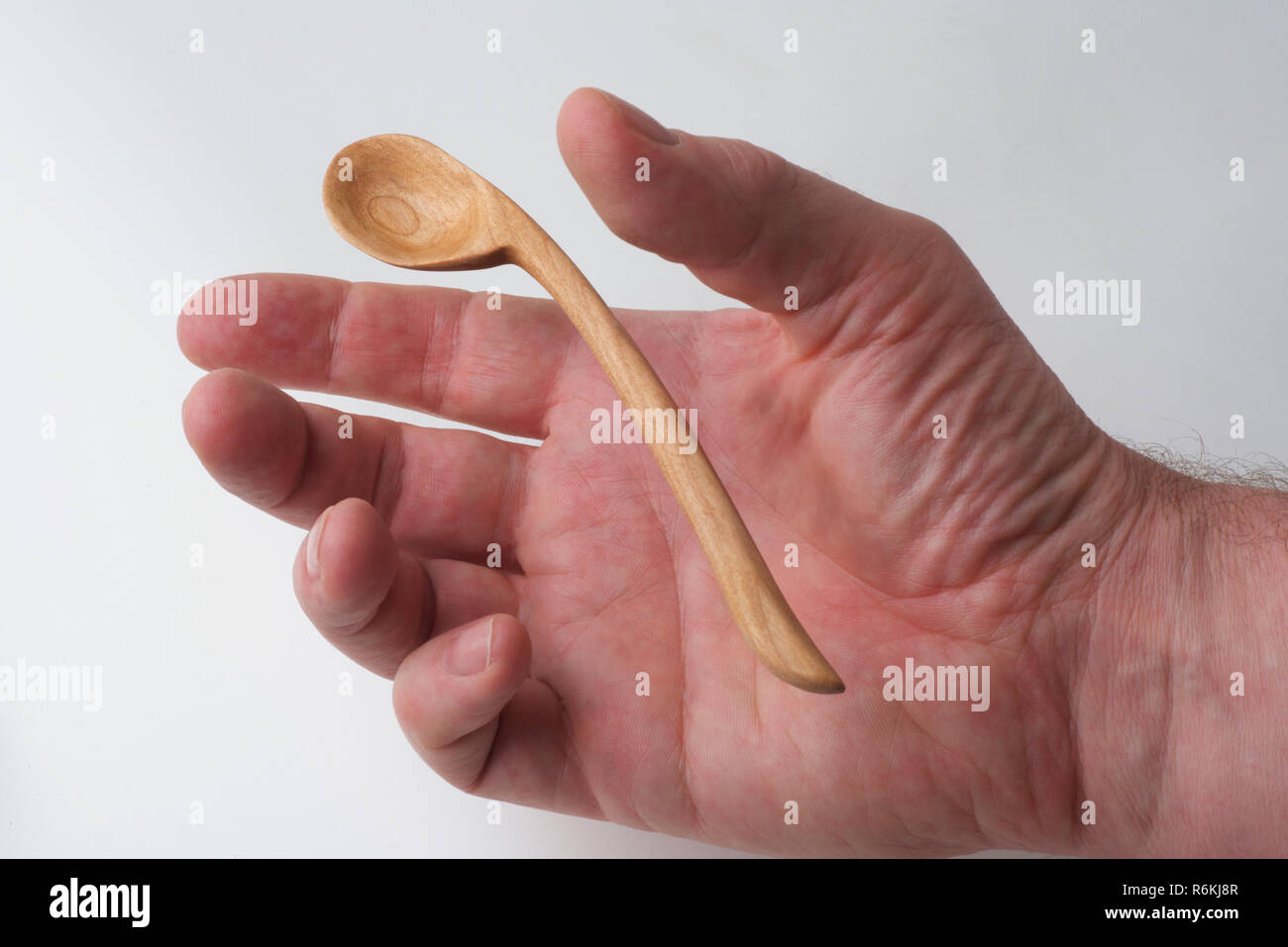 Un maschio raggiunge la mano per afferrare un handmade cucchiaio di legno, contro uno sfondo bianco. Foto Stock