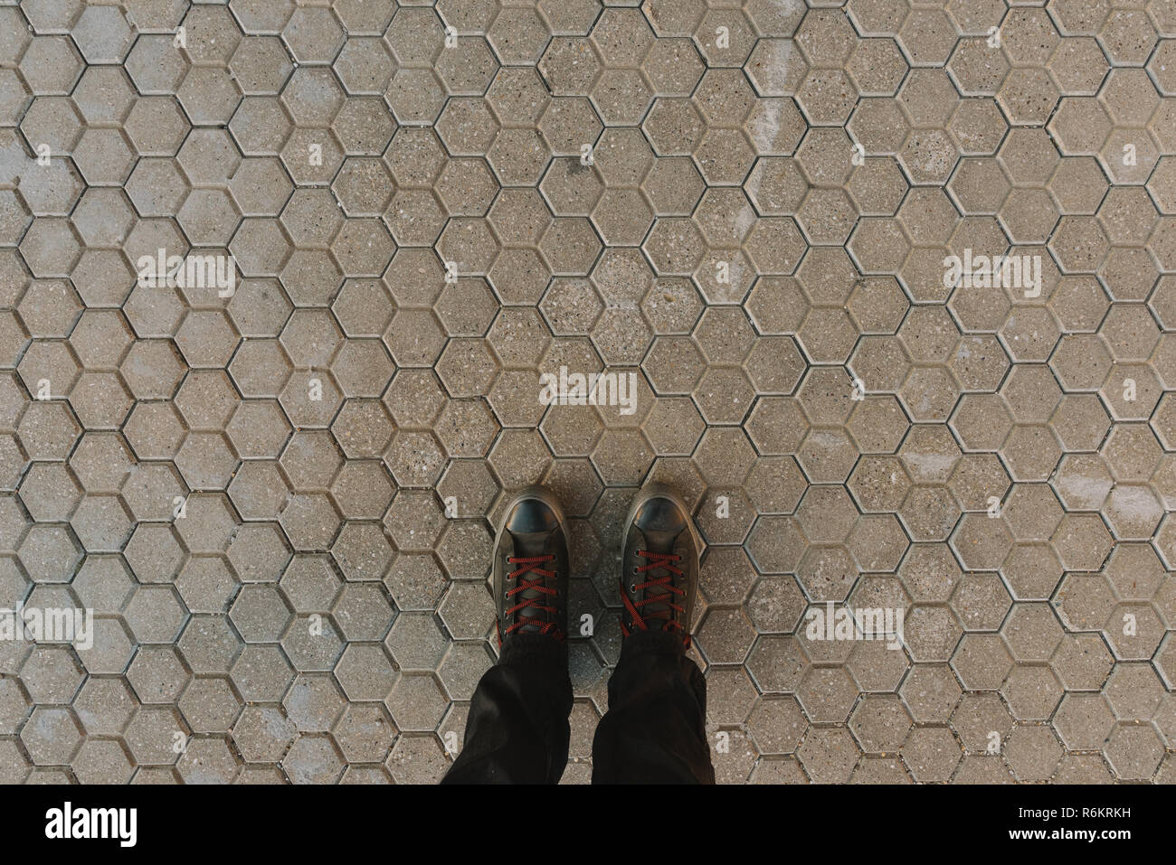 In piedi sul esagonale pavimentazione in calcestruzzo piastrelle sfondo, piedi in scarpe da ginnastica da sopra Foto Stock