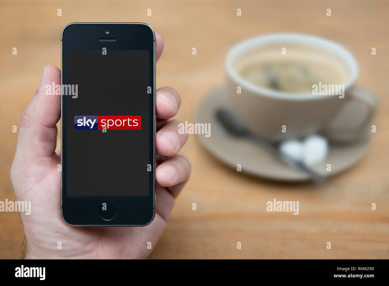 Un uomo guarda al suo iPhone che consente di visualizzare i canali Sky Sports logo (solo uso editoriale). Foto Stock