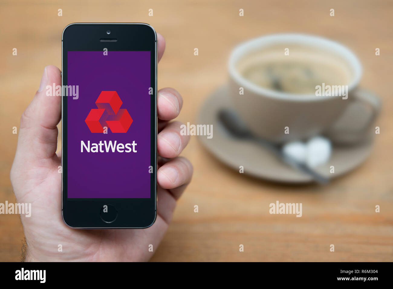 Un uomo guarda al suo iPhone che visualizza la Natwest logo (solo uso editoriale). Foto Stock