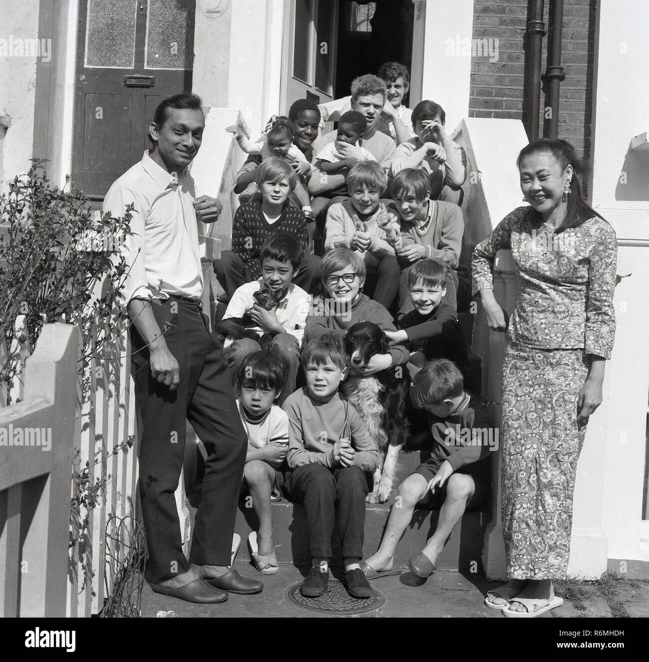 1971, foto storiche di un immigrato il marito e la moglie e la loro grande famiglia adottiva di felice ragazzi,seduti tutti insieme sulle fasi di loro nel sud di Londra Victorian casa a schiera. Insieme con i quindici bambini sorridenti, vi è anche un pet collie cane, molto amato dai più piccoli. Foto Stock
