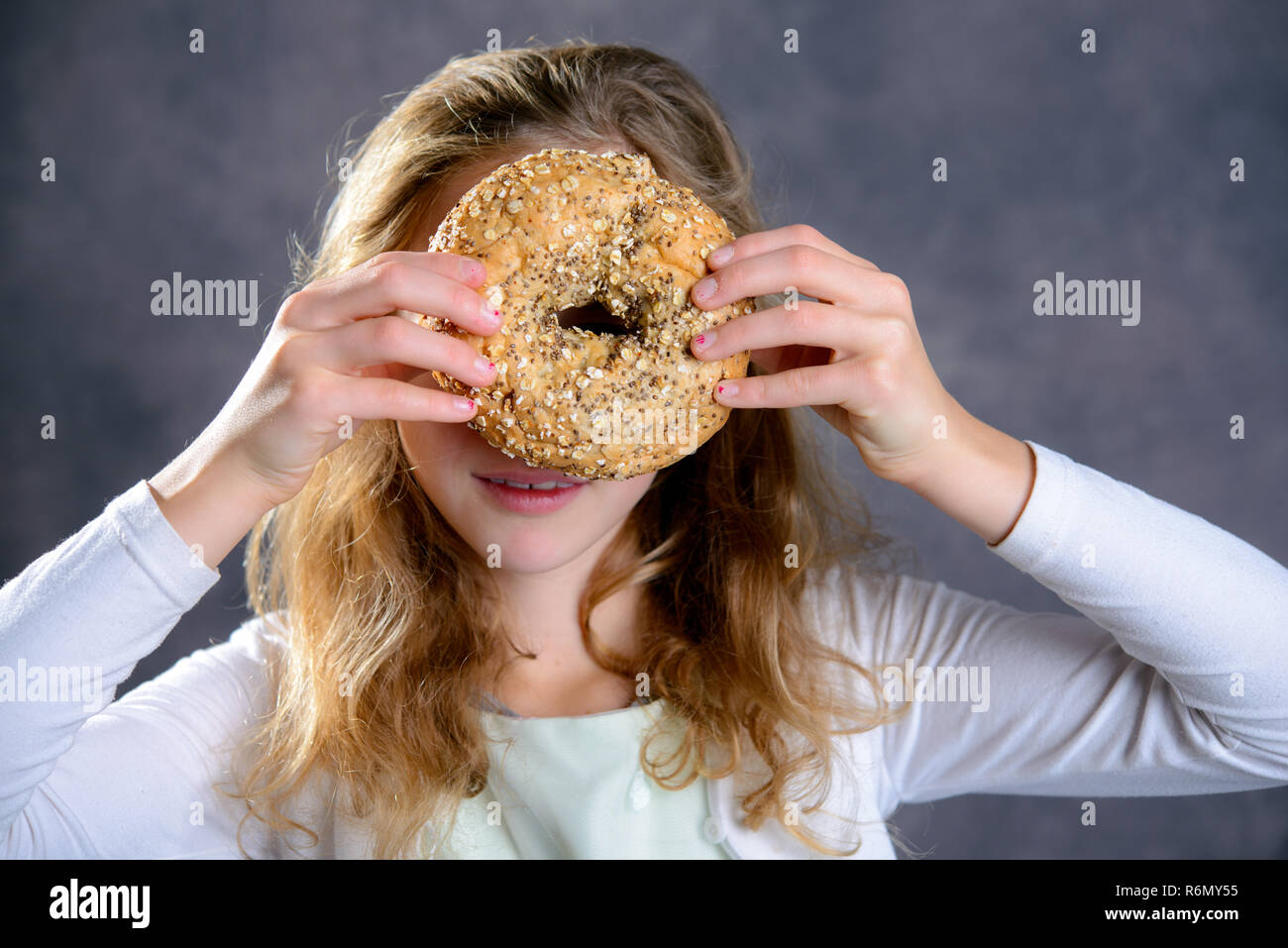 Ragazza bionda guardando attraverso un grande bagel Foto Stock