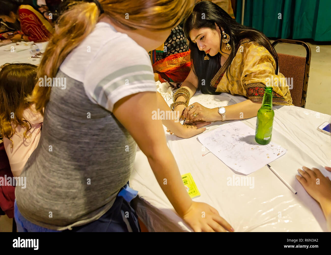 Una donna indiana si applica un Mehndi design per una mano della ragazza con un cono di henné, nov. 17, 2018 al Mobile Festival Internazionale di Mobile, Alabama. Foto Stock