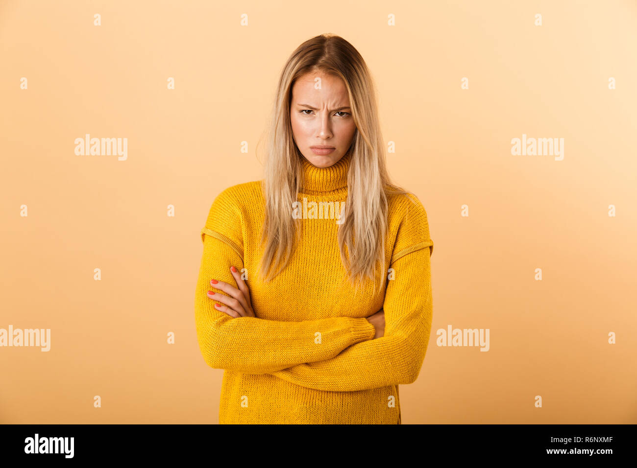 Ritratto di un giovane arrabbiato donna vestita di maglione in piedi isolato su sfondo giallo, tenendo le braccia incrociate Foto Stock
