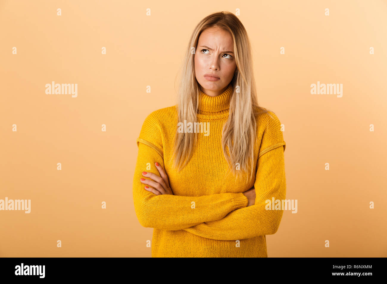 Ritratto di un giovane arrabbiato donna vestita di maglione in piedi isolato su sfondo giallo, tenendo le braccia incrociate, guardando lontano Foto Stock