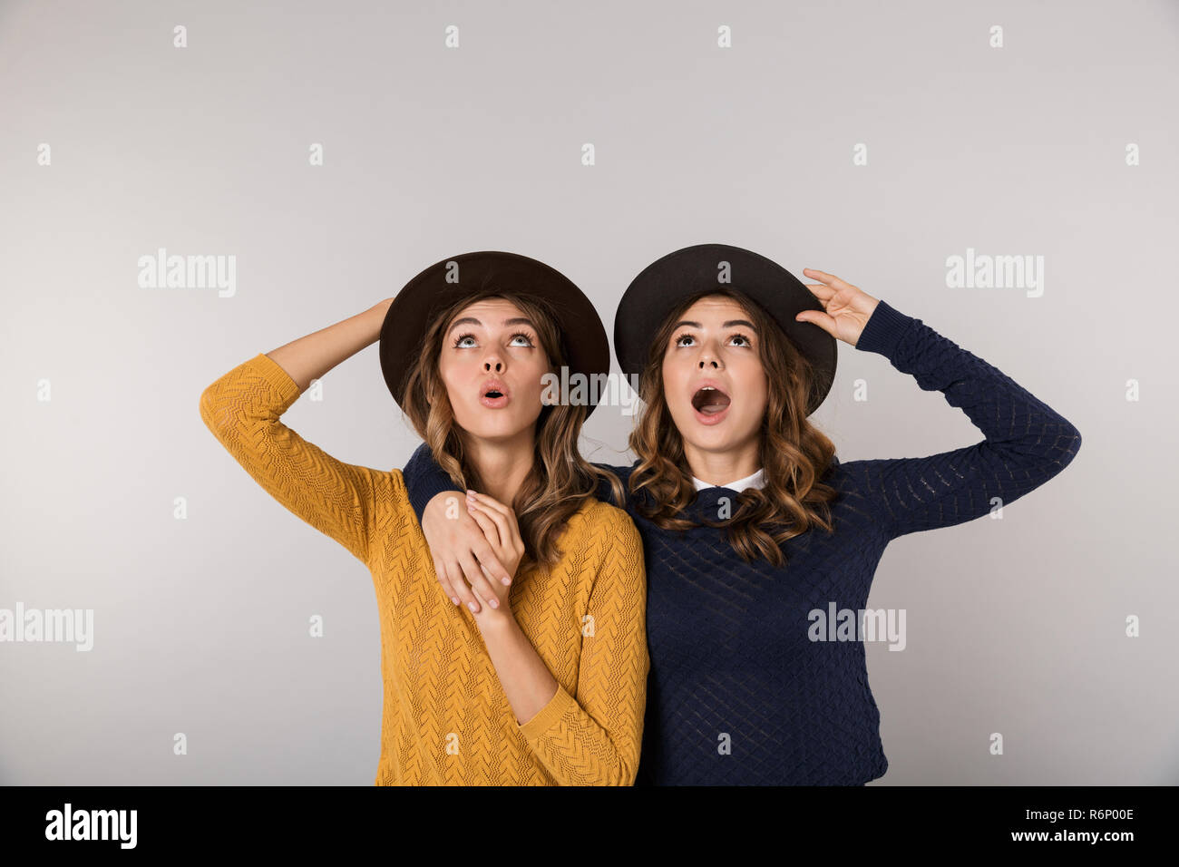 Immagine di due belle donne di indossare cappelli sorridente in telecamera isolate su uno sfondo grigio Foto Stock