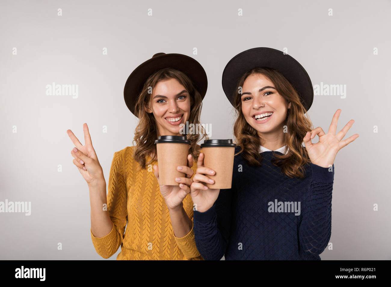 Immagine delle due donne positive indossando cappelli azienda caffè da asporto isolate su uno sfondo grigio Foto Stock