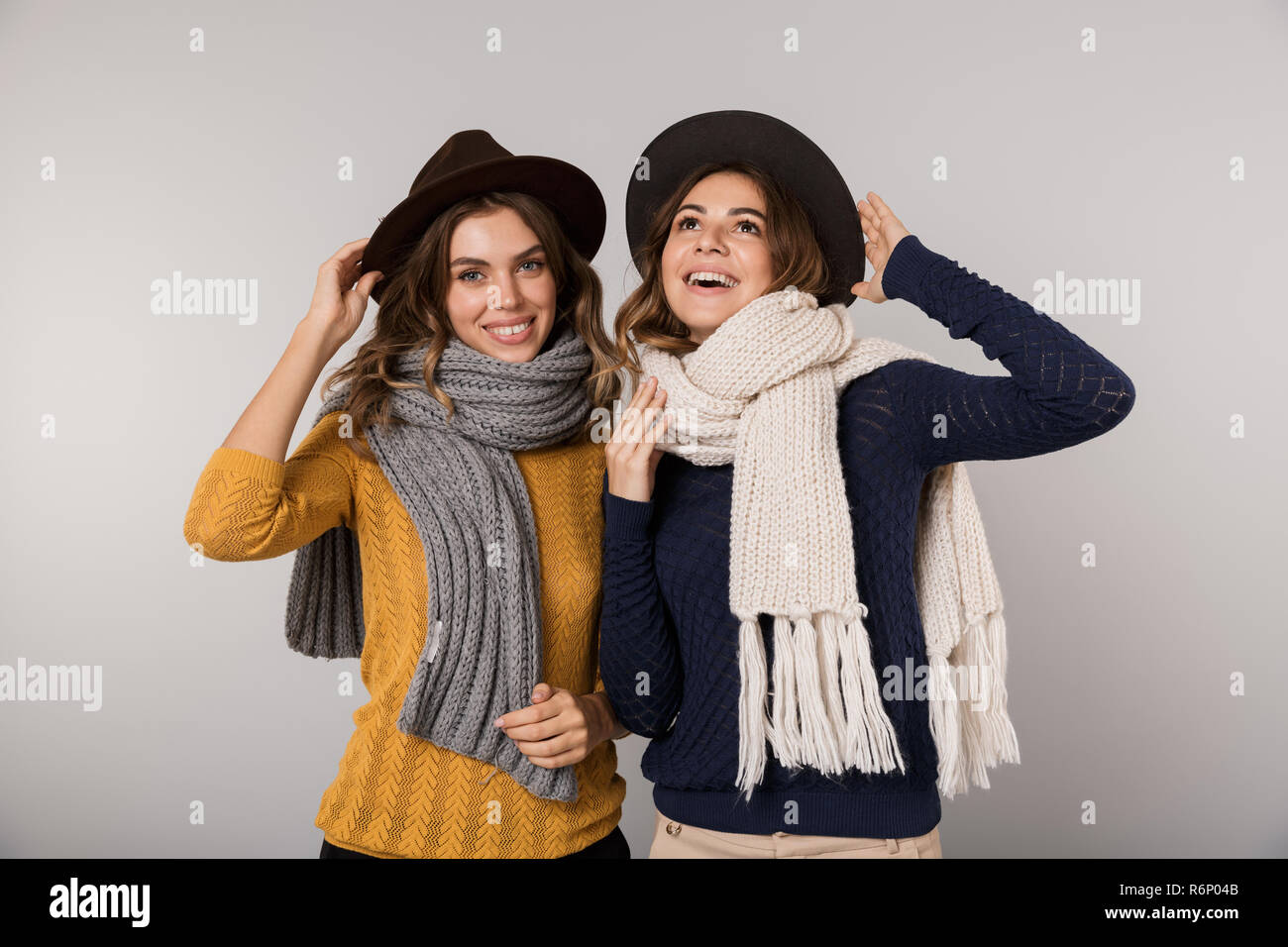 Immagine delle due donne bellissime indossando cappelli e sciarpe sorridente in telecamera isolate su uno sfondo grigio Foto Stock