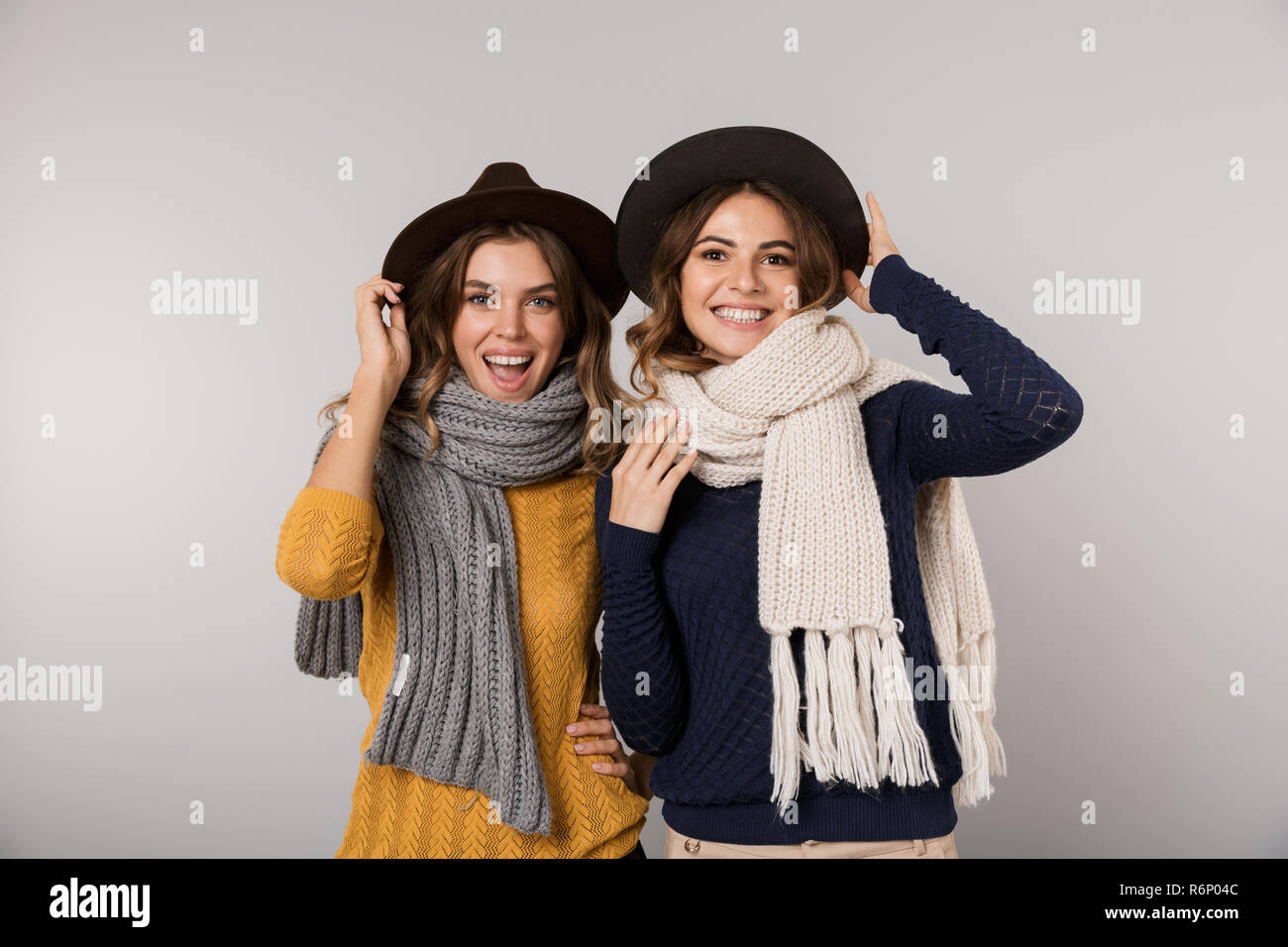 Immagine di due belle donne di indossare cappelli e sciarpe sorridente in telecamera isolate su uno sfondo grigio Foto Stock