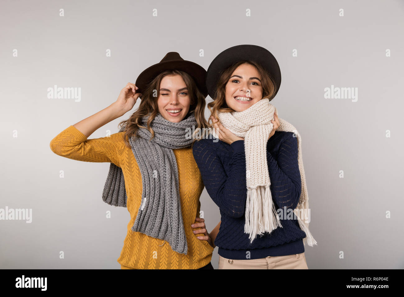 Immagine di due belle donne di indossare cappelli e sciarpe sorridente in telecamera isolate su uno sfondo grigio Foto Stock