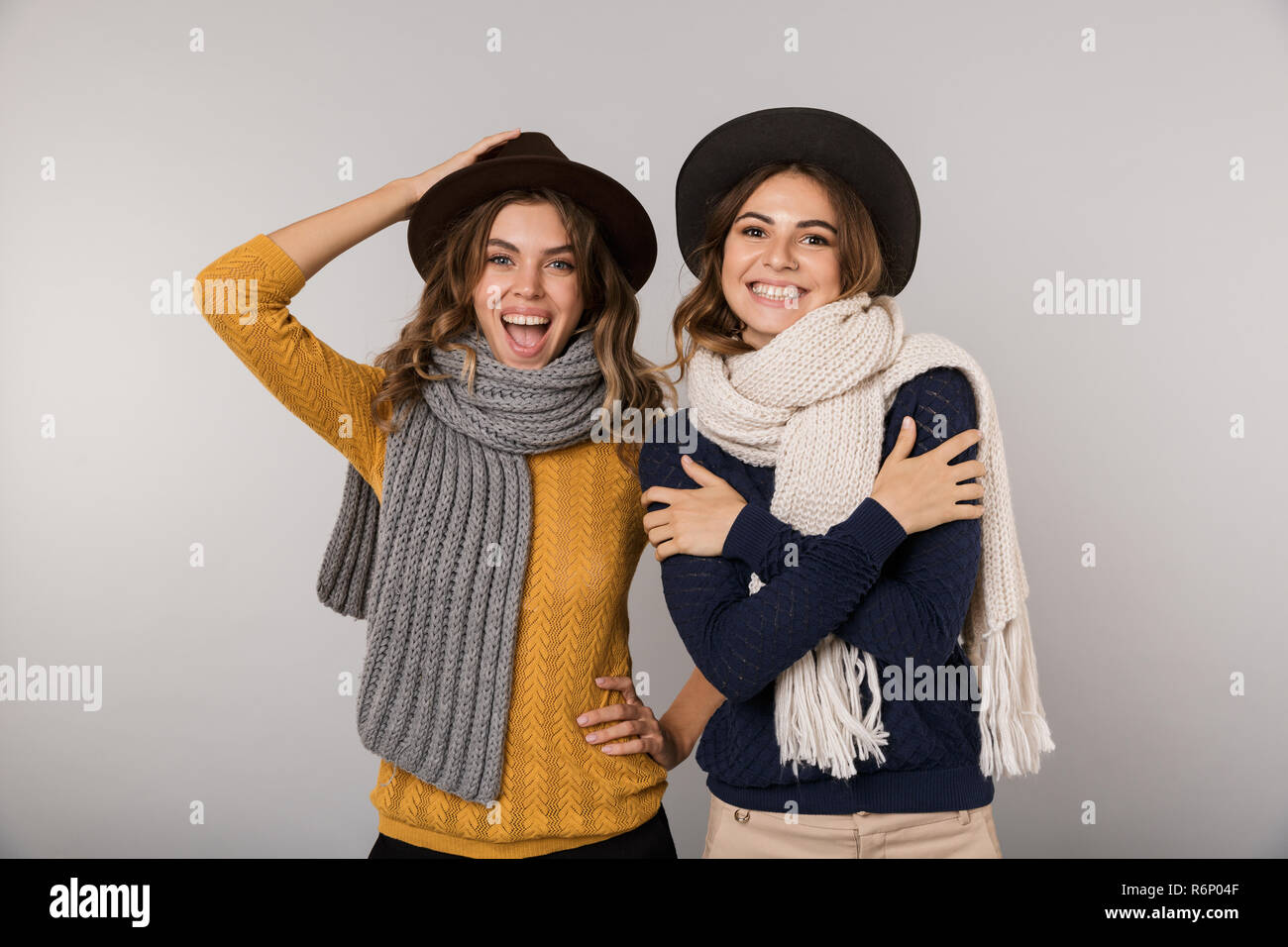 Immagine di due adorabili donne indossare cappelli e sciarpe sorridente in telecamera isolate su uno sfondo grigio Foto Stock