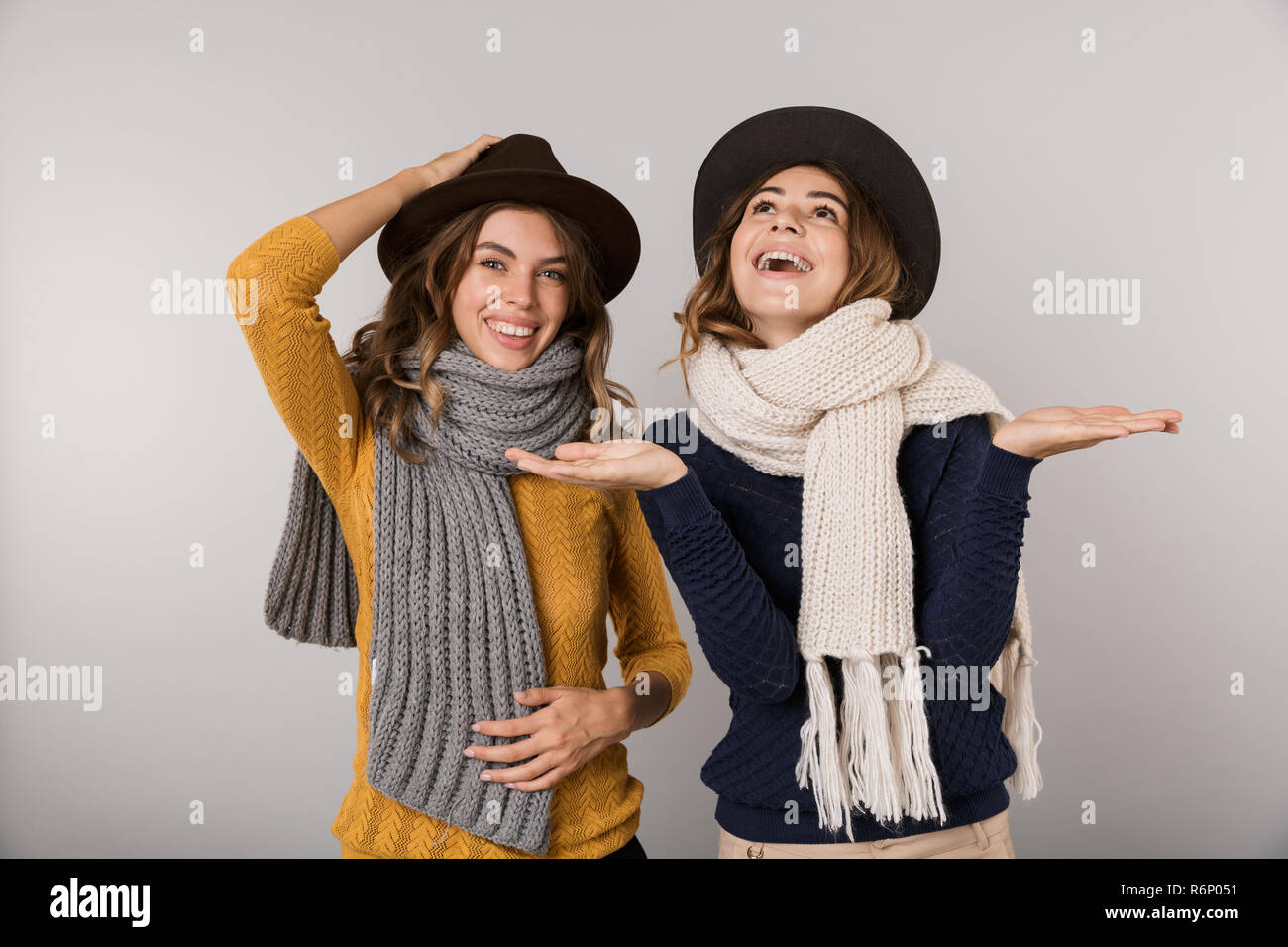 Immagine delle due donne teenage indossare cappelli e sciarpe sorridente in telecamera isolate su uno sfondo grigio Foto Stock