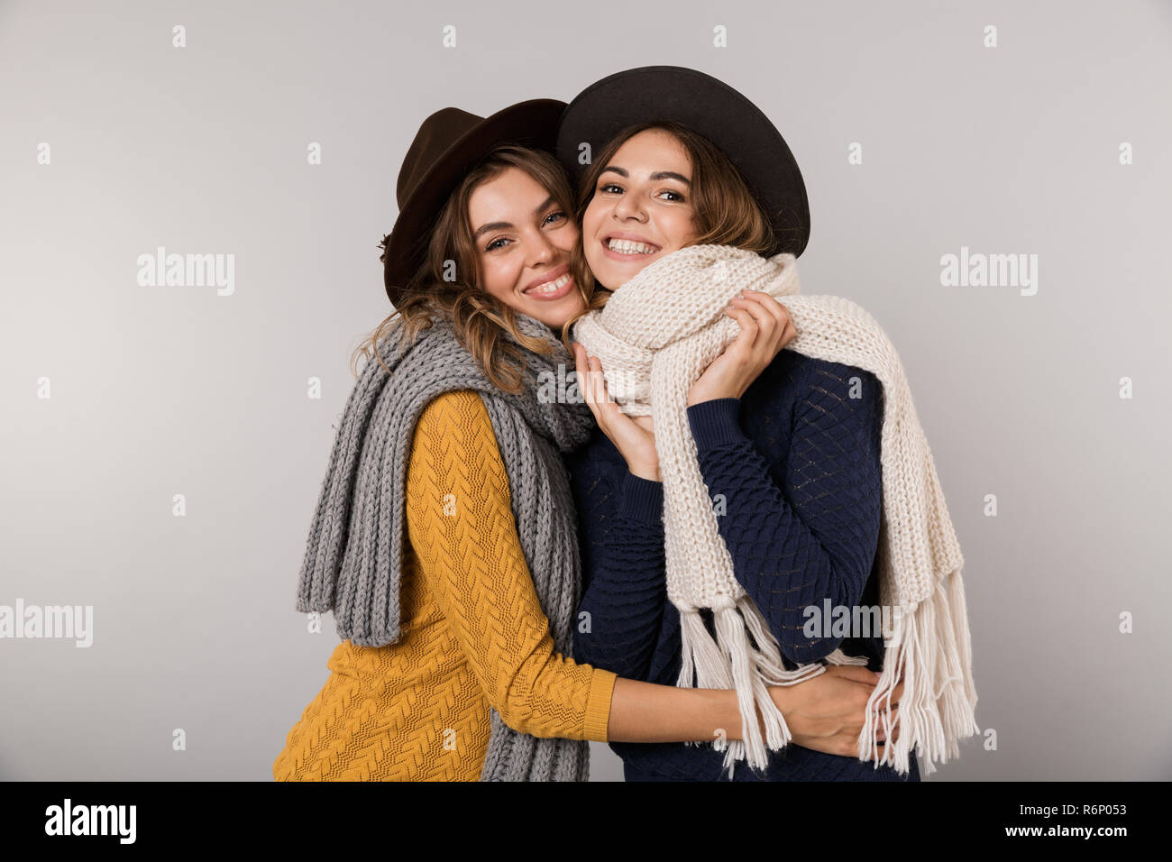 Immagine dei due felici donne indossare cappelli e sciarpe sorridente in telecamera isolate su uno sfondo grigio Foto Stock