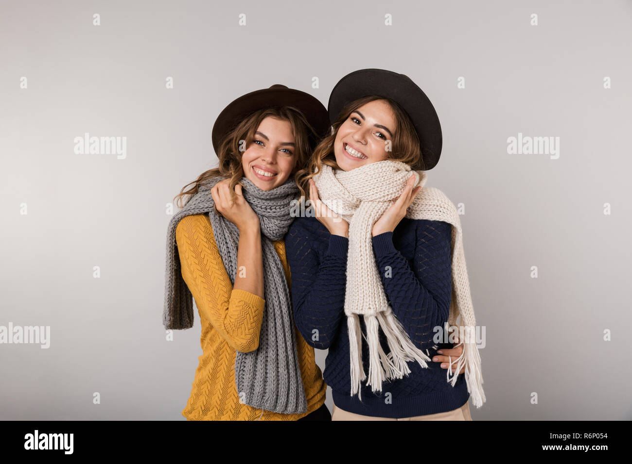 Immagine delle due ragazze piacere di indossare cappelli e sciarpe sorridente in telecamera isolate su uno sfondo grigio Foto Stock