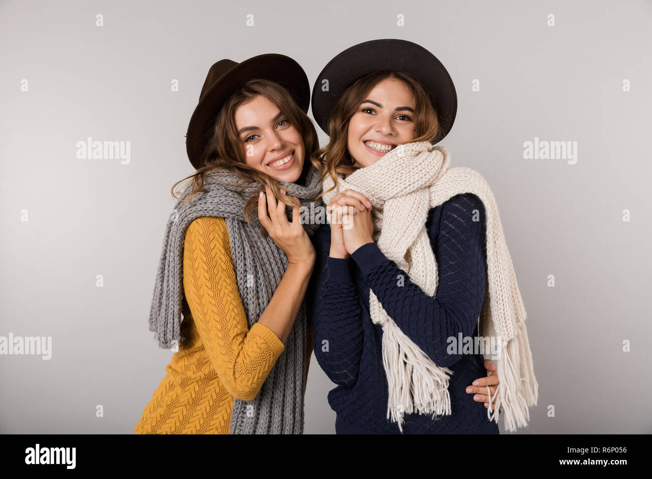 Immagine delle due donne caucasici di indossare cappelli e sciarpe sorridente in telecamera isolate su uno sfondo grigio Foto Stock
