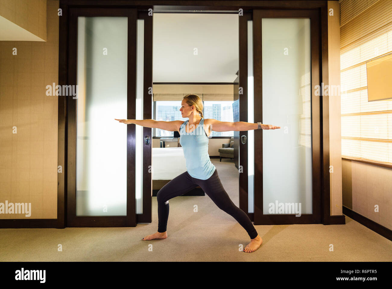Bella donna millenaria pratica lo yoga in camera in hotel in viaggio d'affari Foto Stock