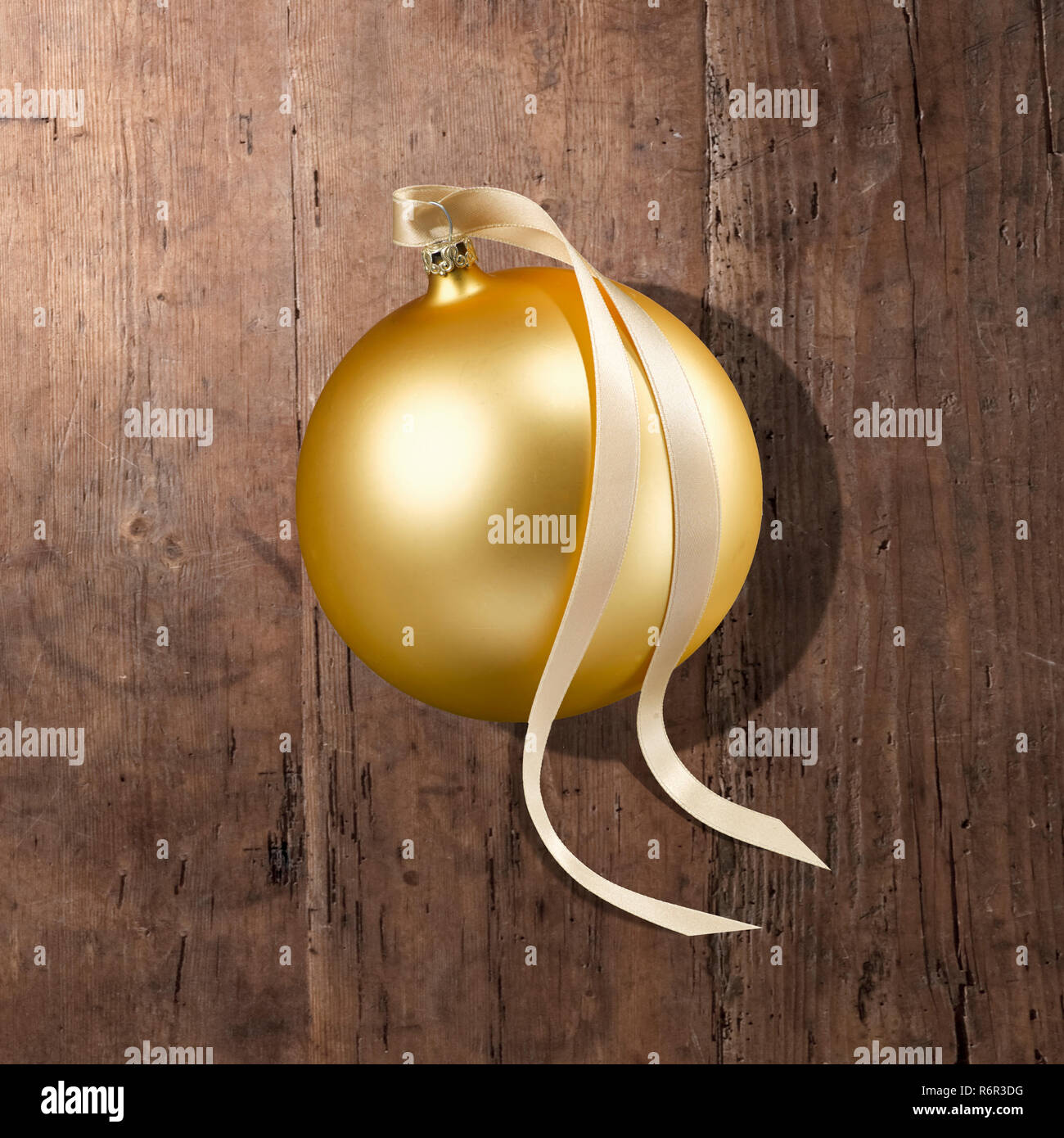 Eine goldene Weihnachtskugel mit Schleifenband, Schattenwurf auf Holzplatte. Foto Stock