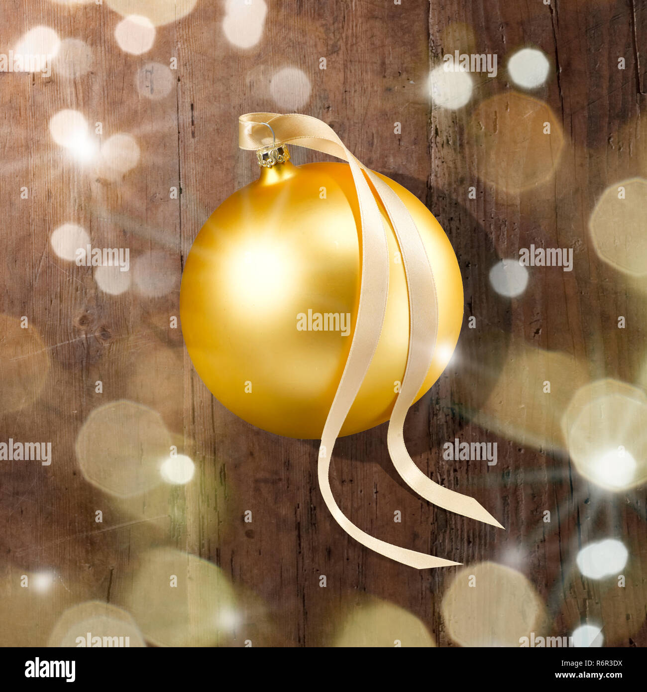 Eine goldene Weihnachtskugel mit Schleifenband, Schattenwurf auf Holzplatte. Lichtreflexe, Lichtsterne und Blendenflecken im Vordergrund. Foto Stock