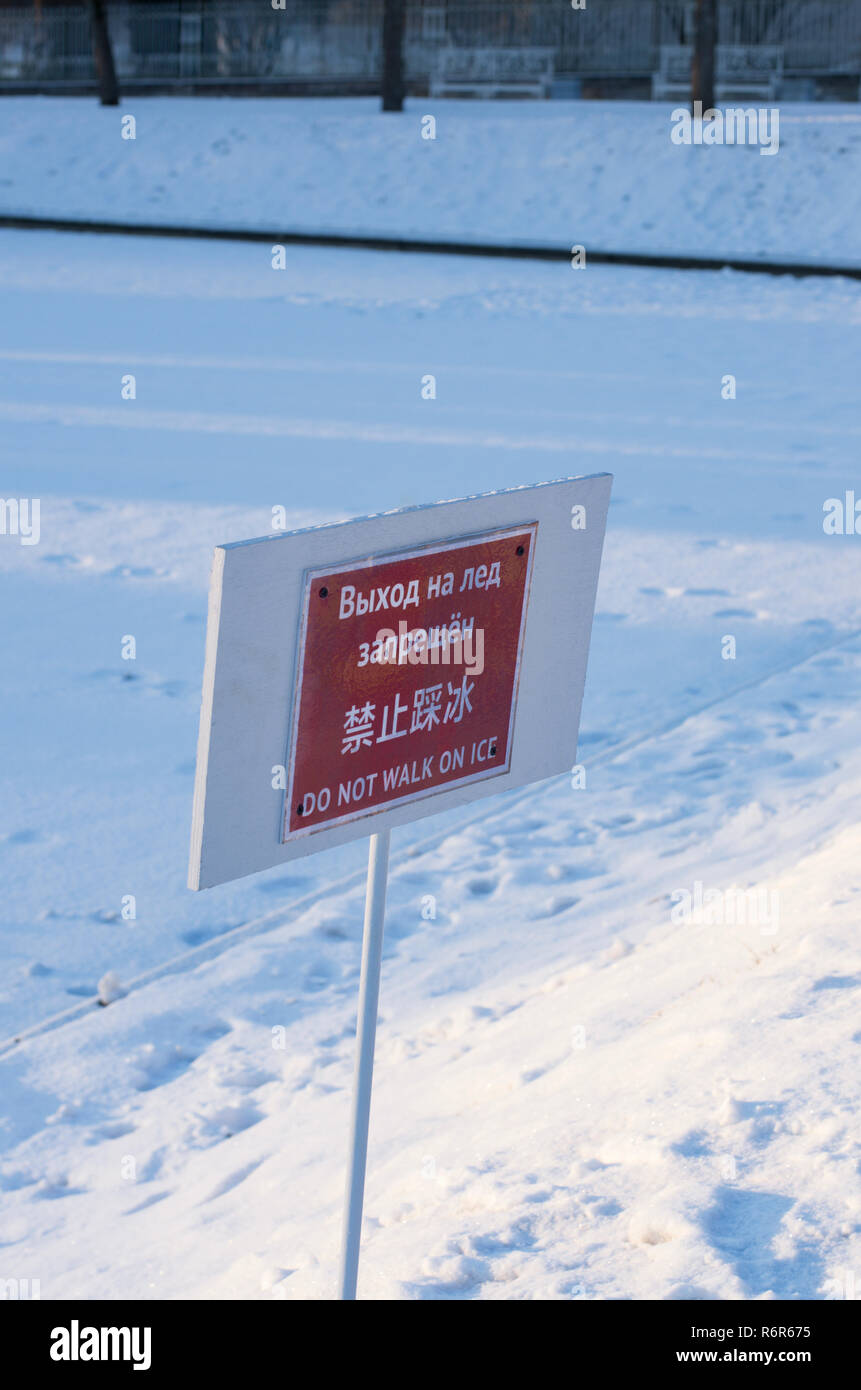 Le informazioni di avvertimento piastra con la scritta 'non camminare sul ghiaccio' in russo, cinese e inglese con impronte sullo sfondo Foto Stock