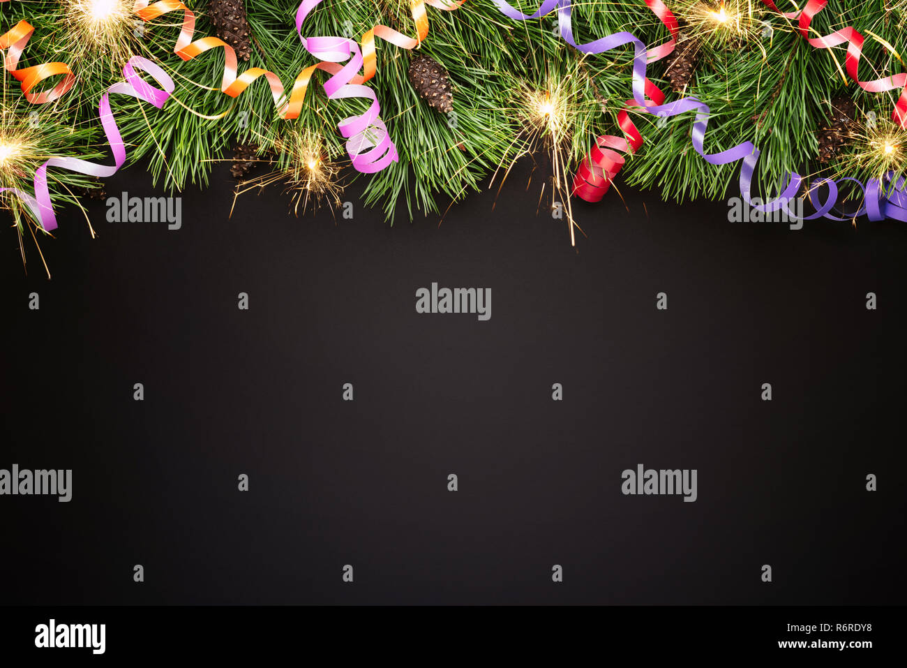 Natale o Capodanno confine con rami di abete e festoso streamers su sfondo nero Foto Stock