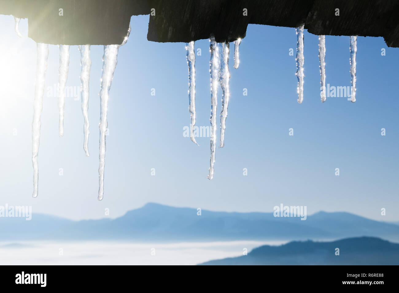Inverno sfondo con ghiaccioli confine. Tempo molto soleggiato con cielo blu e picchi di montagna Foto Stock