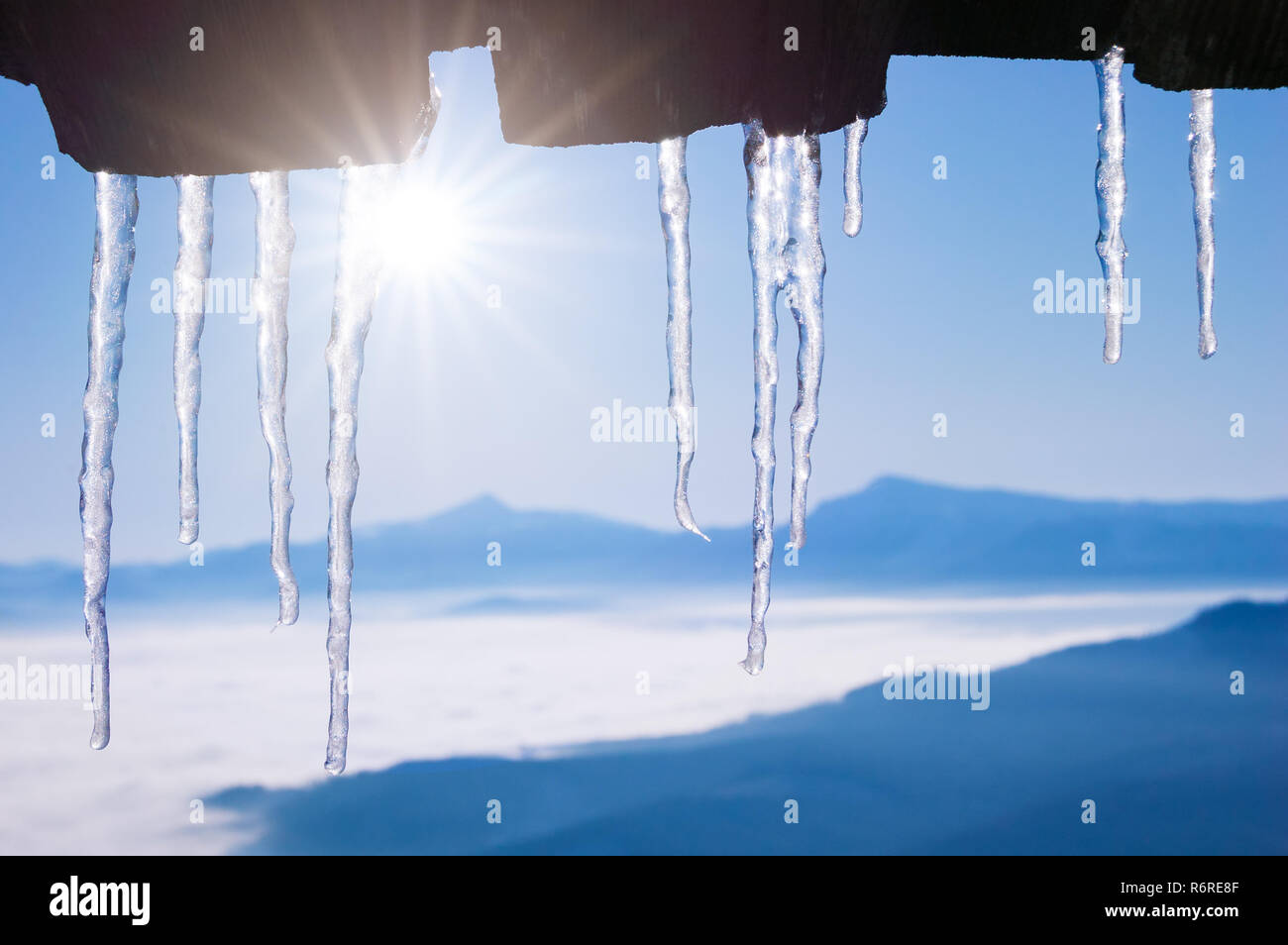 Inverno sfondo con ghiaccioli sul tetto di una casa in legno. Scongelare in un villaggio di montagna. Tempo molto soleggiato con cielo blu Foto Stock