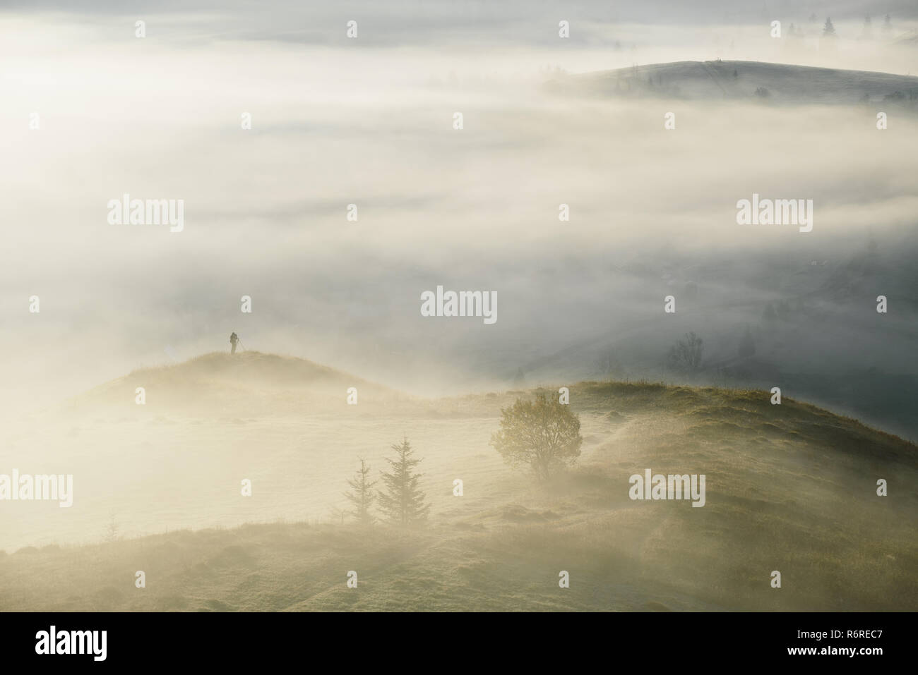 Fotografo di paesaggio con un treppiede in montagna. Mattina nebbia d'autunno. Angolo di Alta Vista dalla collina Foto Stock