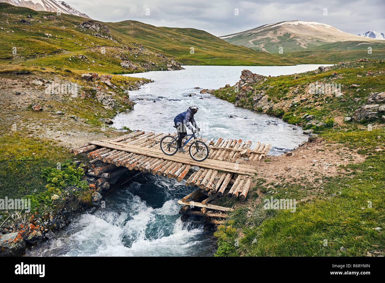 Uomo in mountain bike attraversando il fiume dal ponte di legno nella valle di montagna Foto Stock