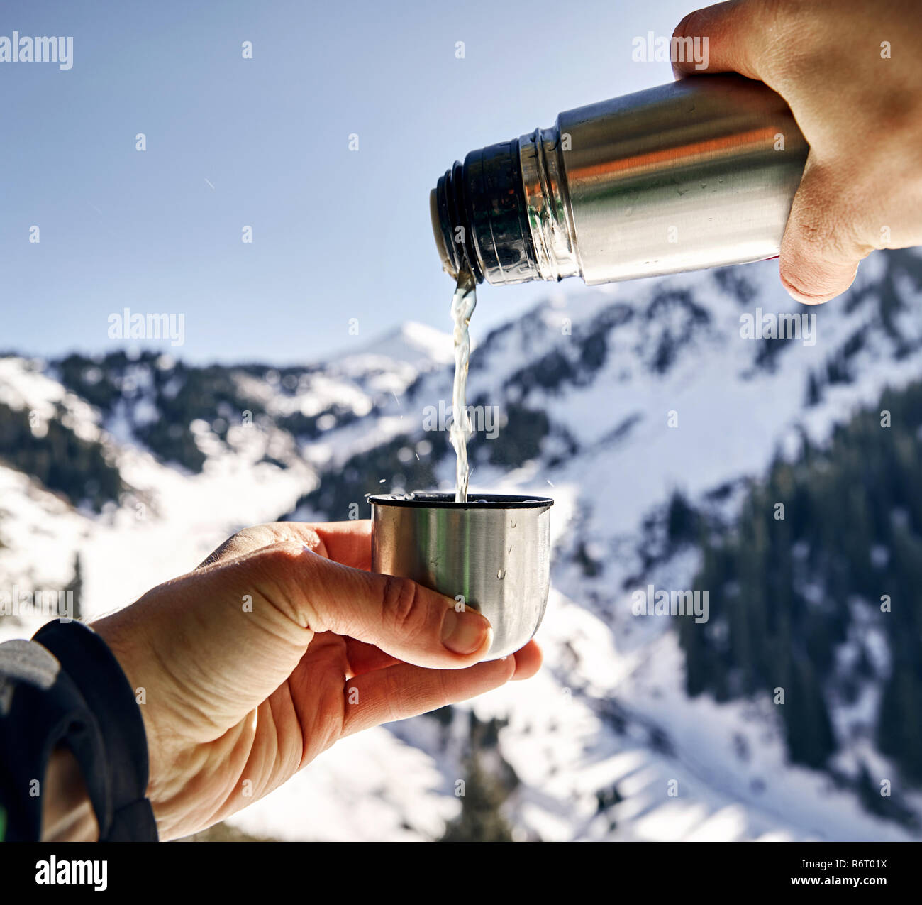 Traveler versando il tè da thermos per tazza contro la montagna invernale dello sfondo. Foto Stock