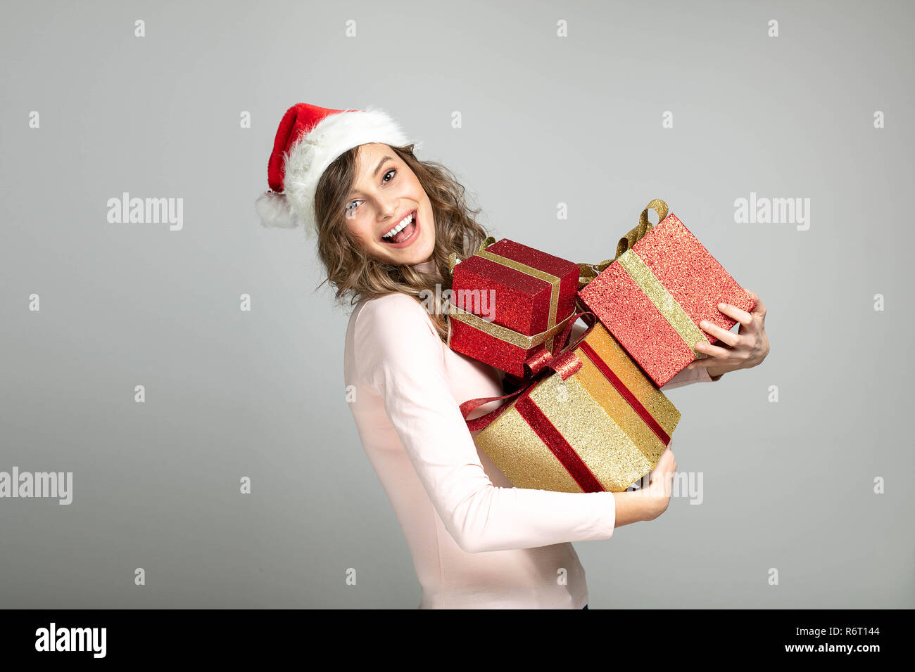 Super eccitati bella donna in maglia rosa e cappello di Natale tenendo un mazzetto di doni in mani, buon natale Foto Stock