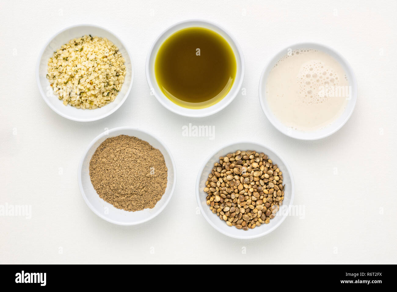 La raccolta di semi di canapa prodotti: cuori, proteine in polvere, latte e olio in piccole ciotole bianco contro arte bianca tela Foto Stock