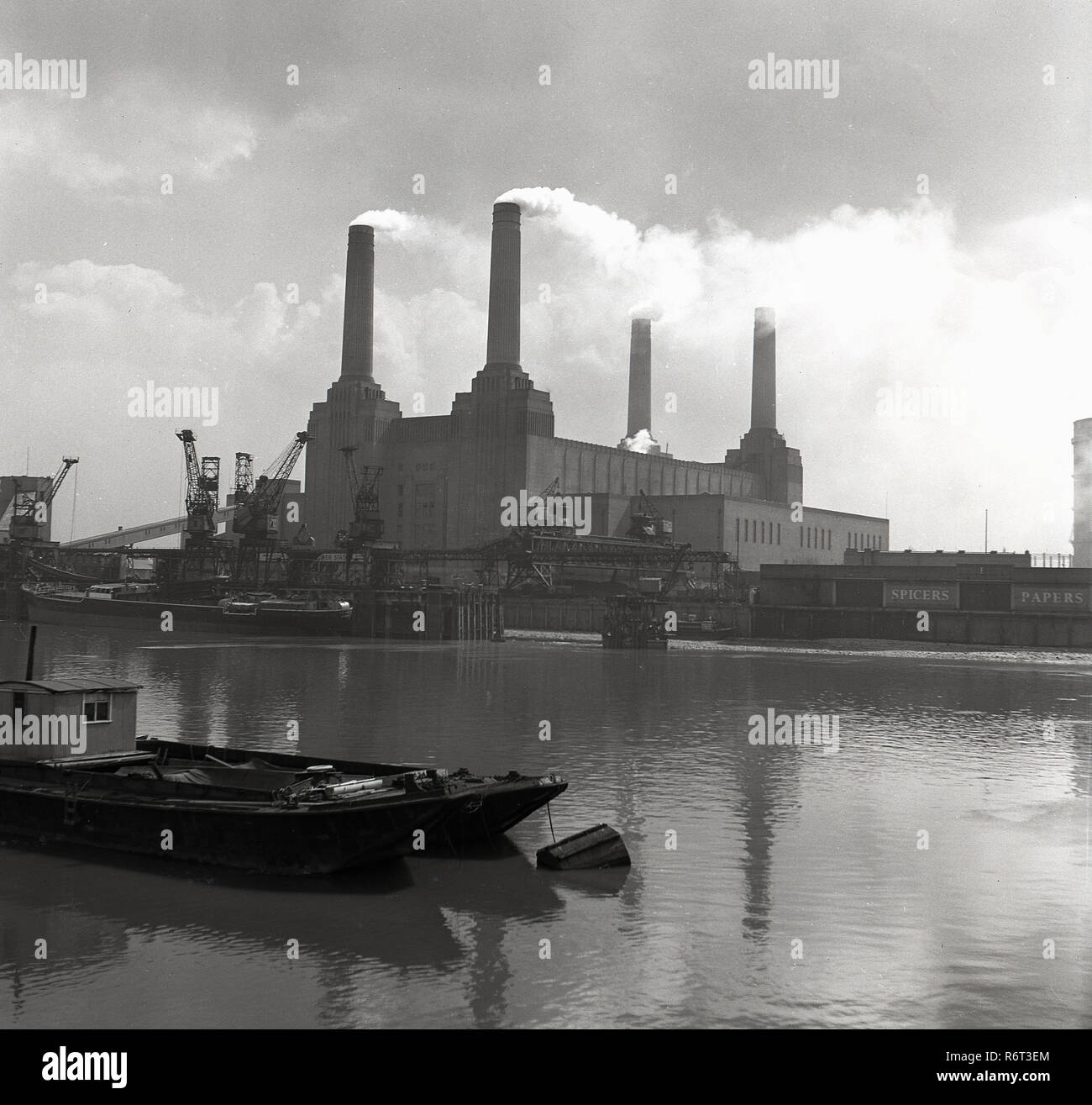 Degli anni Cinquanta, storico, guardando verso sud attraverso il fiume Tamigi, una vista di un gruppo di lavoro di Battersea Power Station , Battersea, Londra, Inghilterra, con fumo emergenti dalla sua iconica quattro camini. Una centrale elettrica a carbone in Nine Elms, Battersea, Wandsworth, fu costruita per il London Power Company e ha iniziato la produzione nel 1933 (una stazione). B Battersea Power Station, costruito tra il 1937-1941 e infine completato nel 1955, è stato costruito per un vicino design identico a "Battersea UN' che conferisce all'edificio è iconico quattro-struttura camino. Foto Stock