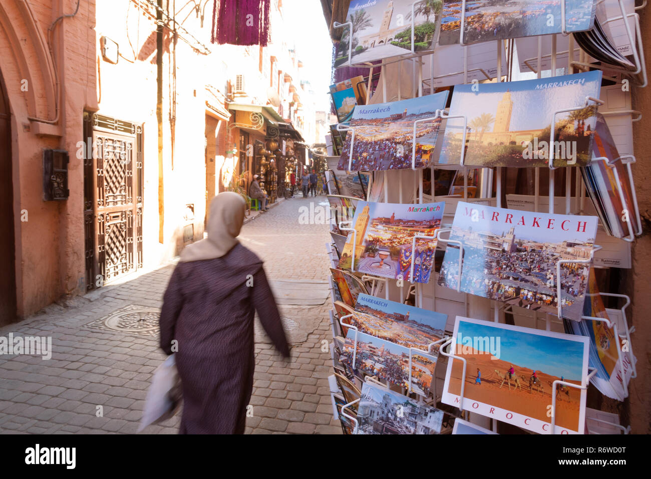 Marrakech turismo - una donna locale cammina davanti a un negozio di vendita di cartoline nel souk, Medina di Marrakesh, Marocco Africa del Nord Foto Stock