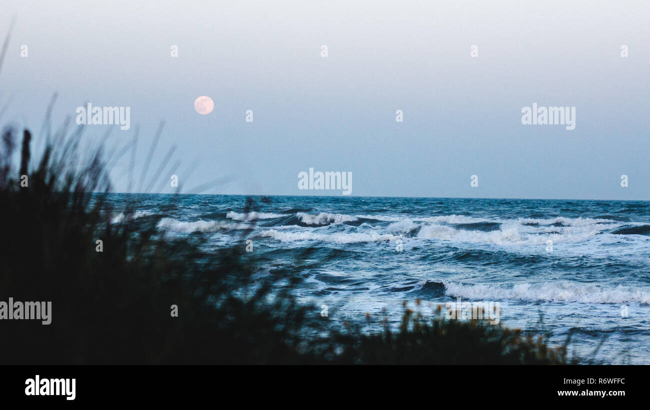 Mare selvaggio con la luna piena in background, concentrarsi sulle grandi onde sulla spiaggia. Foto Stock