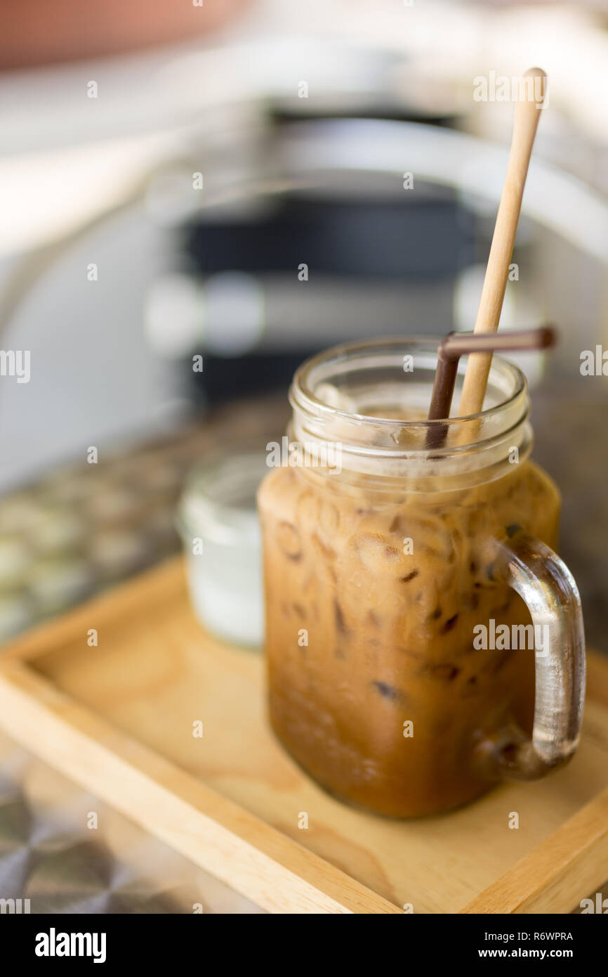 Thai Iced caffè con latte in un bicchiere mason jar sul vassoio in legno e da tavolo, la profondità di campo messa a fuoco. Foto Stock