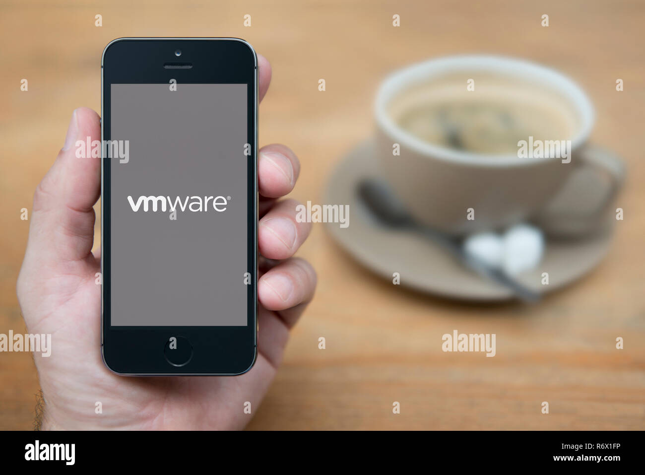 Un uomo guarda al suo iPhone che visualizza le VM Ware logo (solo uso editoriale). Foto Stock