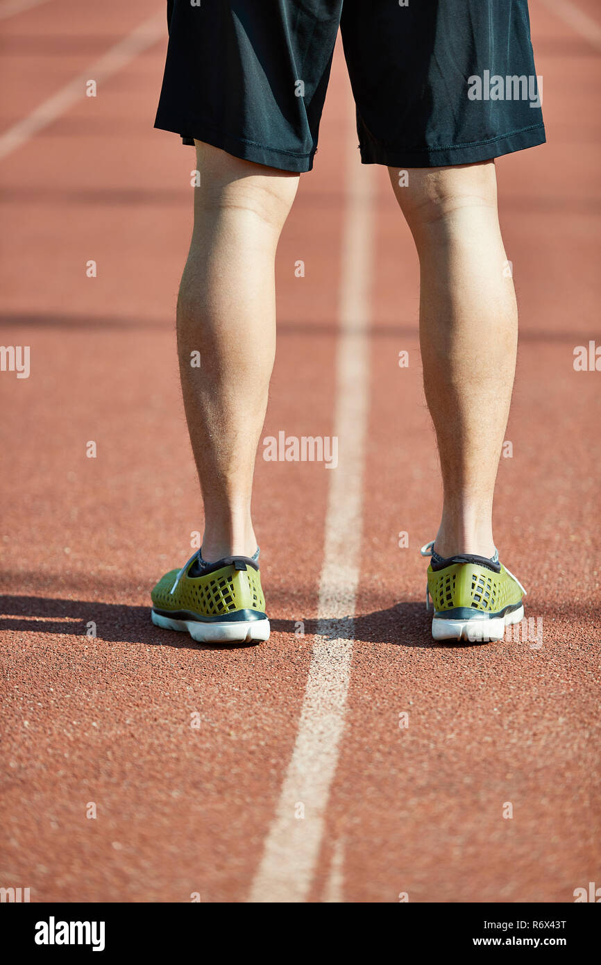 Inquadratura ravvicinata delle gambe e dei piedi di un giovane atleta asiatica permanente sulla pista. Foto Stock