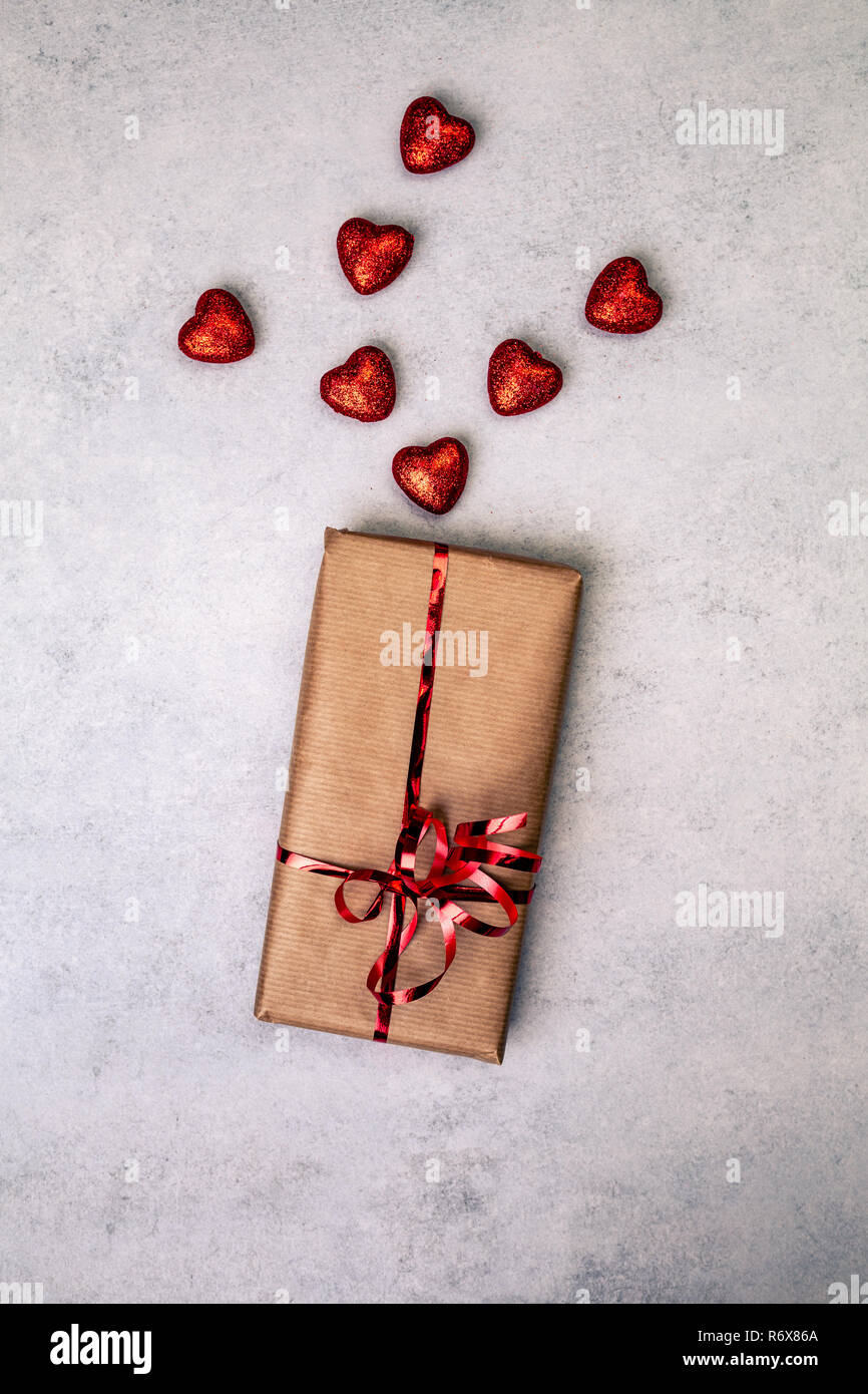 Regalo o presente in carta marrone scatola con cuori rossi. Il concetto di amore su sfondo grigio. Vista dall'alto. con copia spazio. Foto Stock