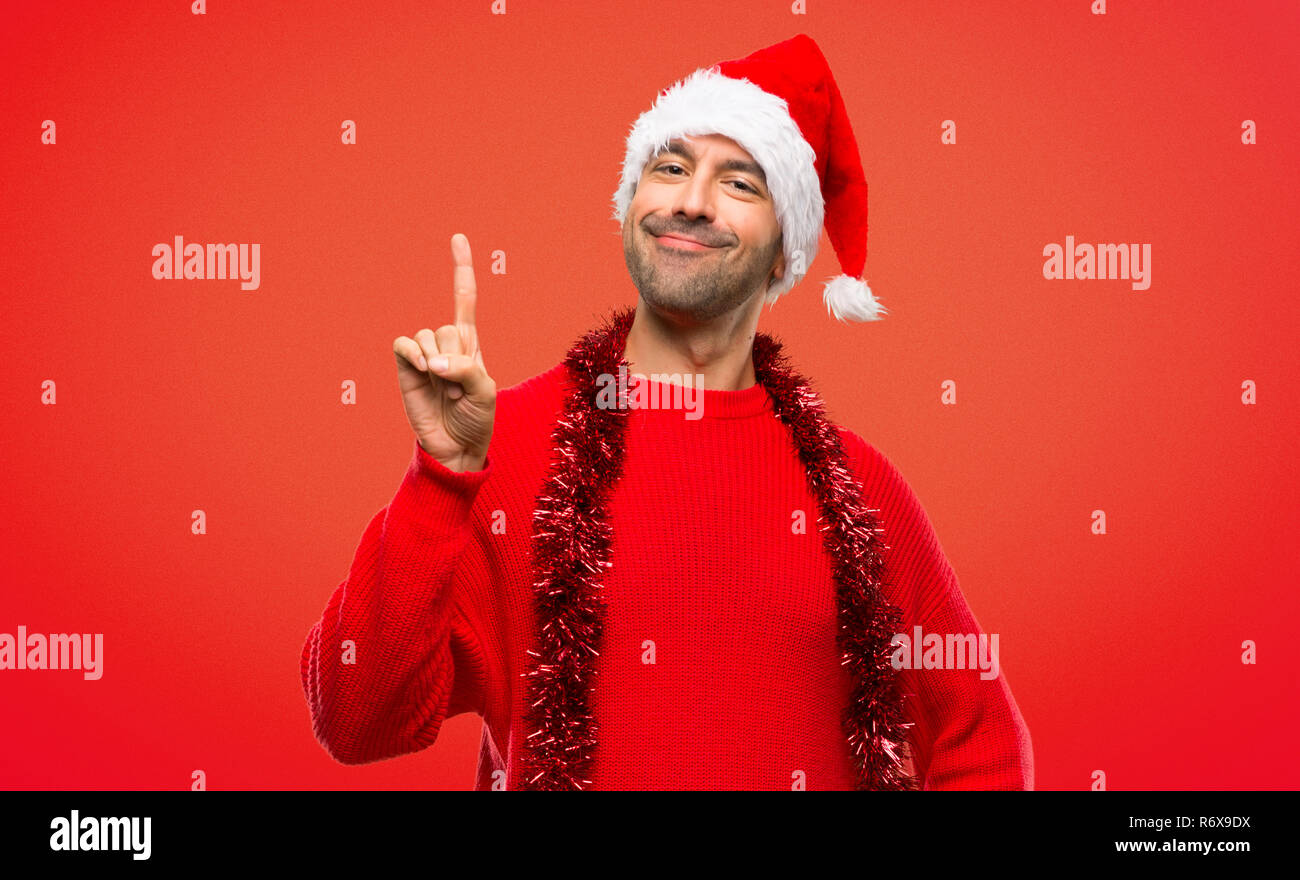 Uomo con vestiti di rosso per celebrare le vacanze di Natale che mostra e sollevare un dito nel segno della migliore su sfondo rosso Foto Stock