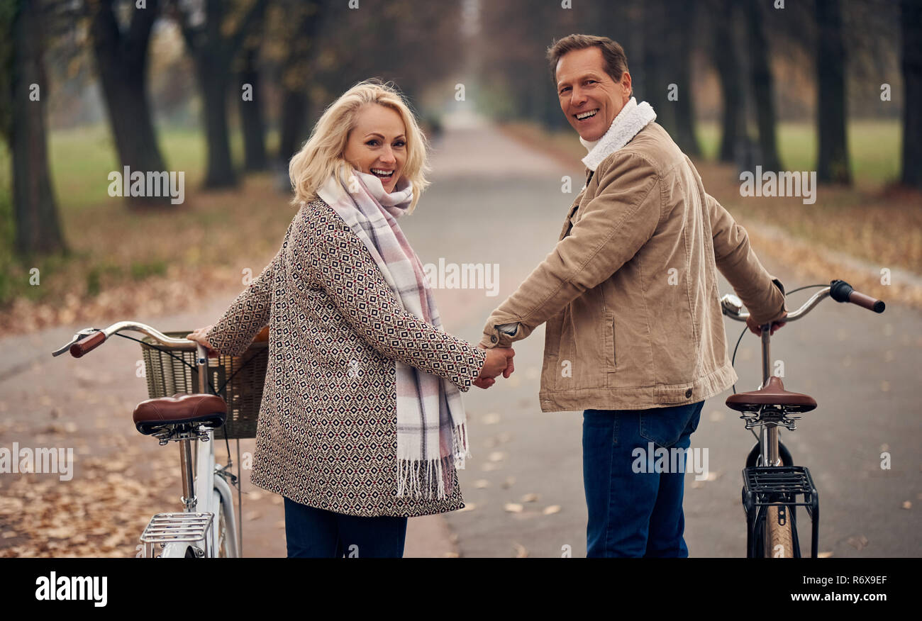 Coppia senior passeggiate nel parco in autunno. Attraente donna e uomo bello trascorrere del tempo insieme con le biciclette Foto Stock