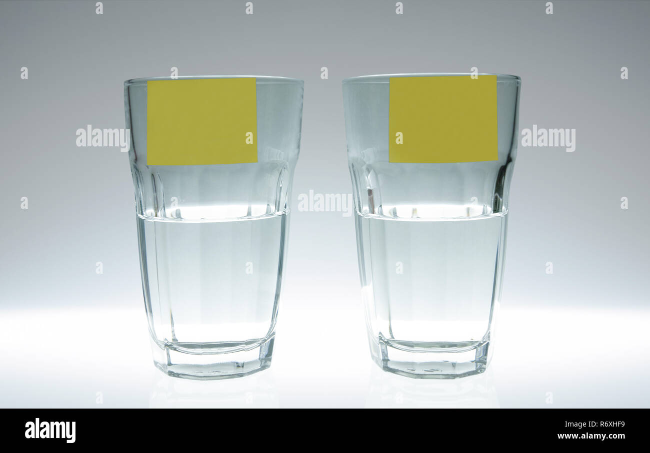 Due bicchieri di acqua: una piena a metà, l'altra mezza vuota. Su ciascuna lastra di vetro vi è un post-it. Foto Stock