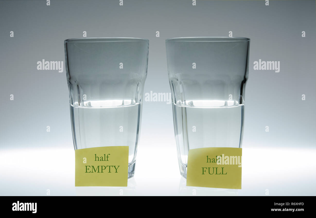 Due bicchieri di acqua: una piena a metà, l'altra mezza vuota. Nella parte anteriore di ciascuna lastra di vetro vi è un post-it. Foto Stock